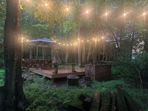 A wooden deck with a table and bench, surrounded by trees and string lights. - Majestic, private cabin with hot tub/multiple deck...a little taste of heaven! (Dahlonega)