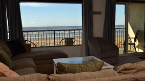 A living room with a view of the beach, a sofa, a chair, and a glass coffee table. - Oceanfront 4th floor, Balcony with Spectacular Ocean Views (Seaside)