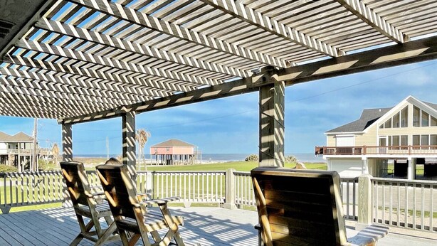 A wooden deck with a chevron-patterned pergola, overlooking a beach and a house. - PORTKEY - 2nd Row, Beach view, 4 bedroom, Sleeps 12 (Crystal Beach)