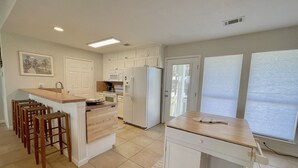 A kitchen with a central island, bar stools, a refrigerator, and a microwave. - PORTKEY - 2nd Row, Beach view, 4 bedroom, Sleeps 12 (Crystal Beach)