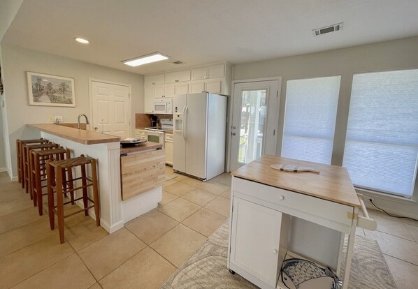 A kitchen with a central island, bar stools, a refrigerator, and a microwave.