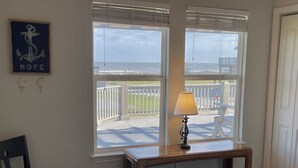 A bedroom with a bed, a chair, a nightstand with a lamp, and a view of the ocean through large windows. - PORTKEY - 2nd Row, Beach view, 4 bedroom, Sleeps 12 (Crystal Beach)