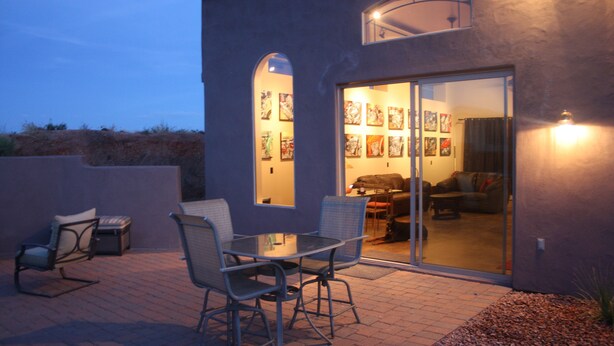 An outdoor patio with a table and chairs, a sliding glass door leading to an interior space with artwork on the walls. - The motorsport studio (Cave Creek)