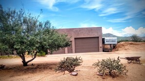 A building with a garage door, surrounded by desert vegetation and a wheelbarrow. - The motorsport studio (Cave Creek)