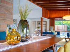 A wooden table with three glass vases, one containing green plants, and a brick wall in the background.