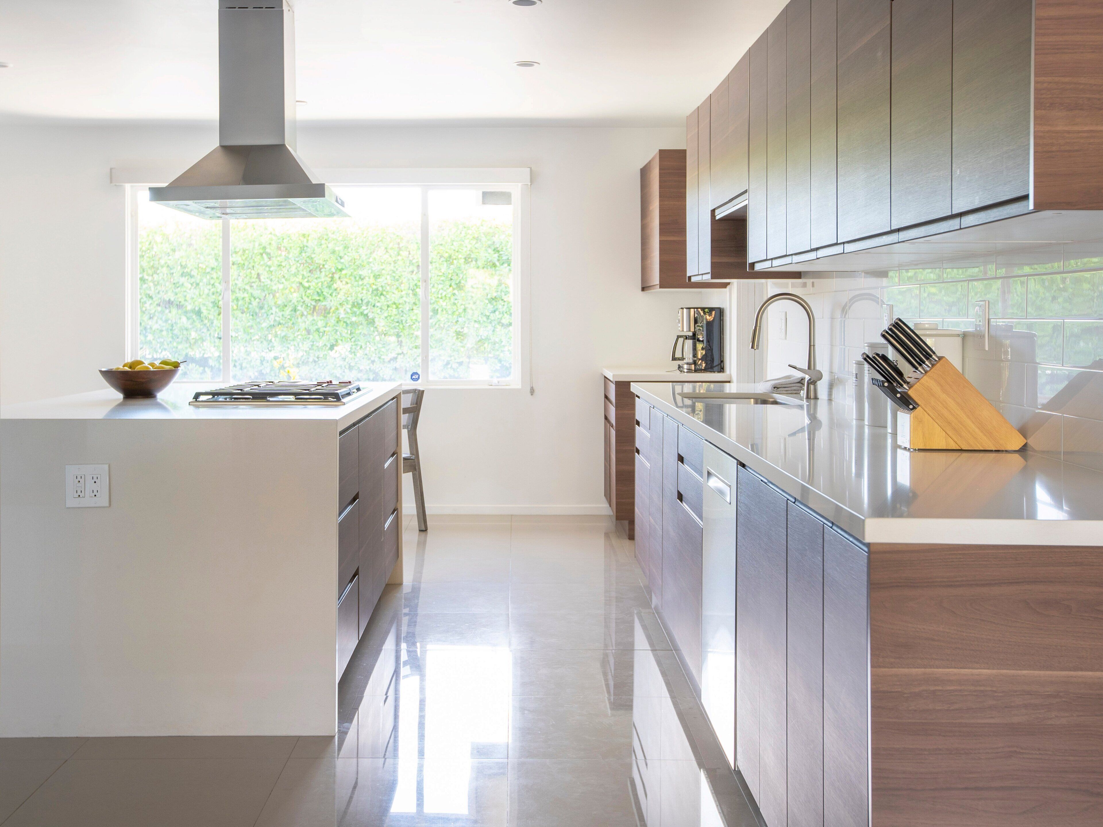 A modern kitchen with an island, stainless steel appliances, and a view of greenery outside.