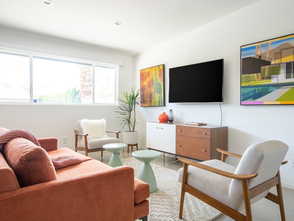 A modern living room with a sofa, armchairs, a coffee table, a TV, and artwork on the wall.