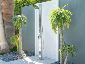 Une cabine de douche moderne, ornée d’un motif géométrique, entourée d’une base en béton et de petits galets.