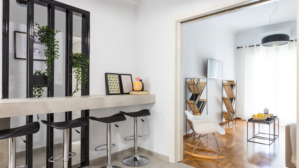 A modern kitchen with a bar area, featuring black bar stools, a large mirror, and decorative plants. - Special Prices Urban Athens Apartment 2 min walk from metro (Athina)