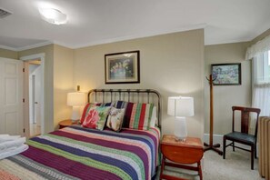 Une chambre à coucher avec un lit, deux lampes de chevet, une chaise et deux tableaux encadrés accrochés au mur.