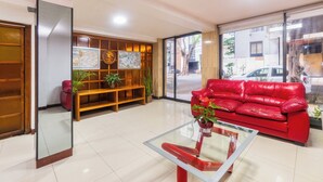 A modern lobby with a red leather sofa, a glass coffee table, and a wooden reception desk. - Capital O Hotel Suites Marne, Mexico City (Mexico City)