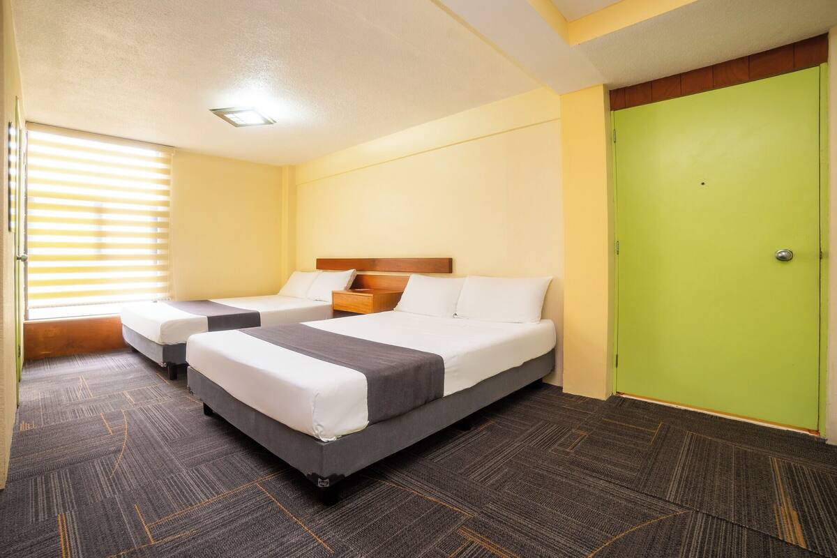 A hotel room with two beds, a green door, and a window with blinds.
