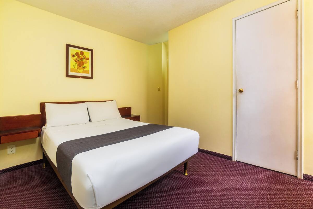 A hotel room with a bed, a nightstand, a door, and a framed picture on the wall.