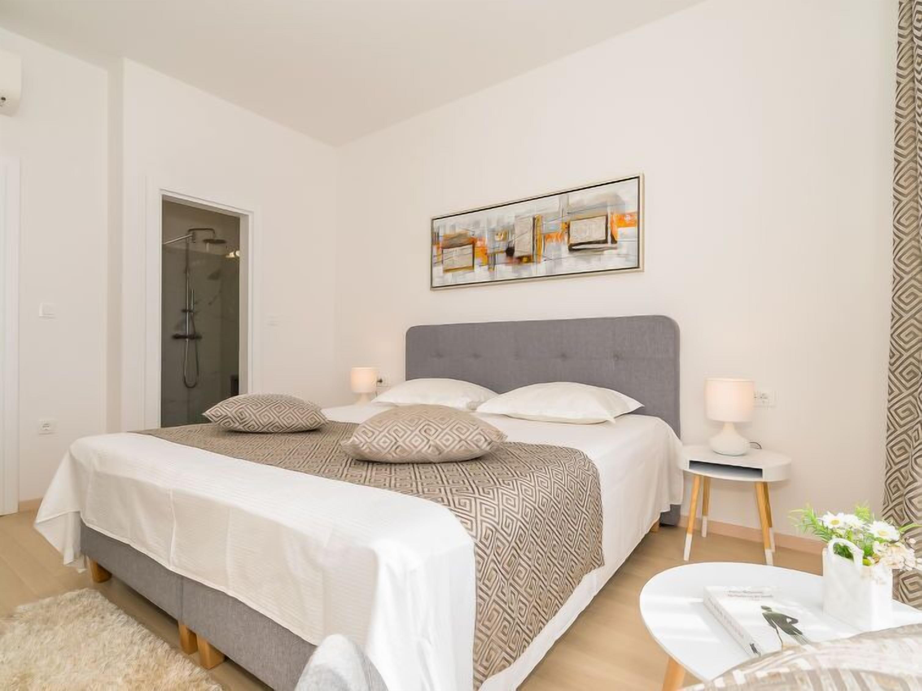 A modern bedroom with a large bed, a shower, a bedside table with a lamp, and a framed picture on the wall.