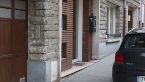 En bygning med en murstensfacade, en trædør og en sort bil parkeret foran.