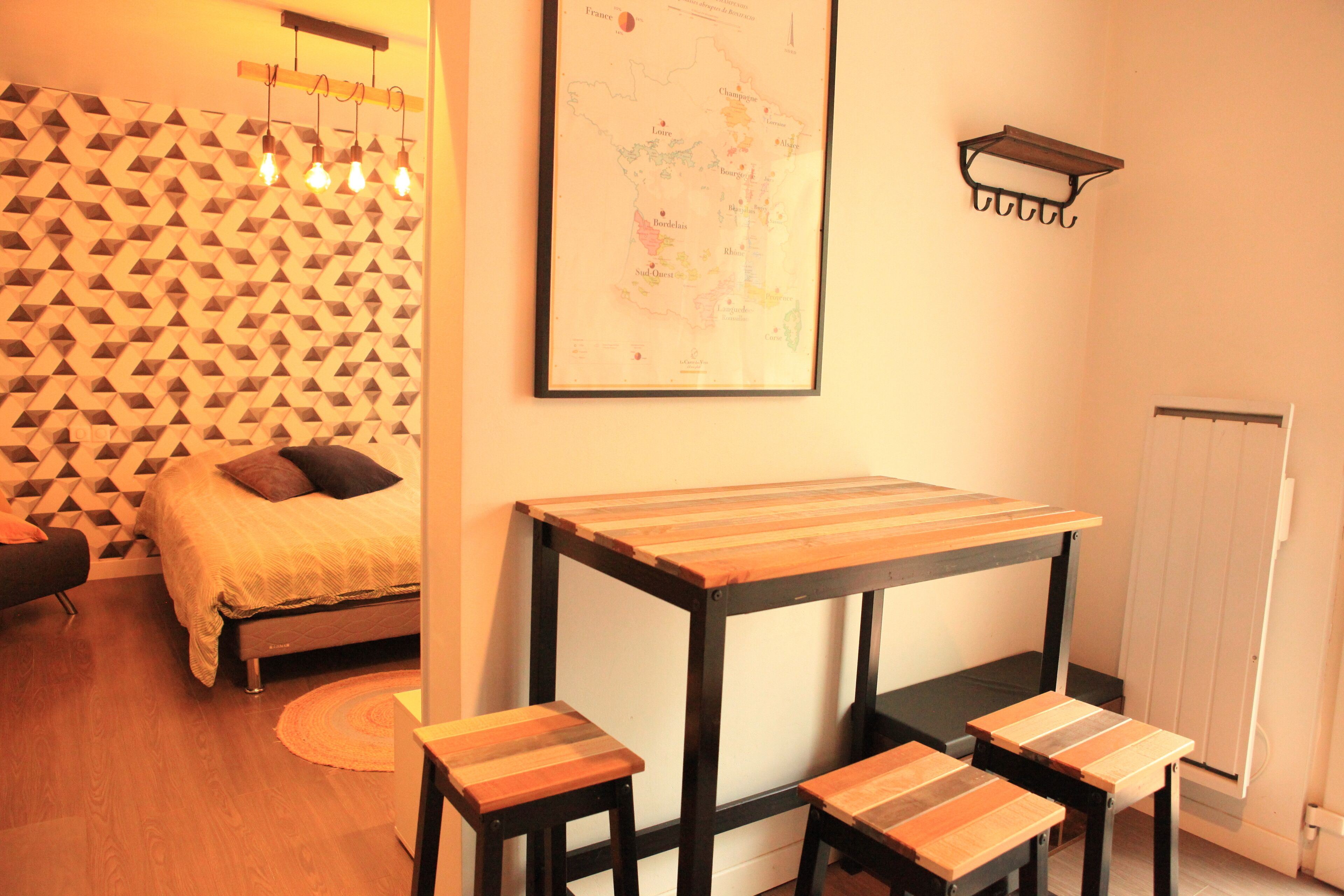 Une chambre avec un lit, une carte accrochée au mur, une table en bois avec des tabourets et un mur orné d’un motif géométrique.