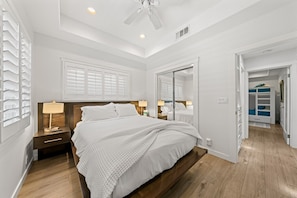 Une chambre à coucher comprenant un lit, des tables de chevet, un ventilateur de plafond et un dressing.
