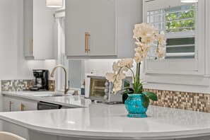 Une cuisine moderne avec des meubles blancs, un ßlot central, une machine à café et un vase décoratif contenant une orchidée.