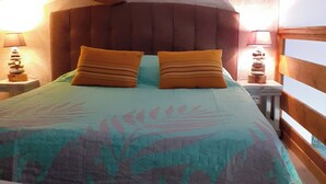 A bed with a patterned bedspread, two pillows, a wooden headboard, and bedside lamps. -  Holiday rental Gite Pousada Tropical (VOLVENT)