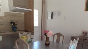 A dining area with a wooden table and chairs, a vase with flowers, and a kitchen in the background. -  Holiday rental Gite Pousada Tropical (VOLVENT)