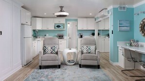 Une cuisine avec des meubles blancs, un îlot central, deux fauteuils et un tapis d écoratif.