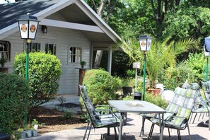 Eine Terrasse mit Tisch und Stühlen, umgeben von Grünpflanzen und einem Haus.