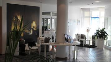 A modern hotel lobby with a large painting of a cityscape, a round white table, and comfortable seating areas.