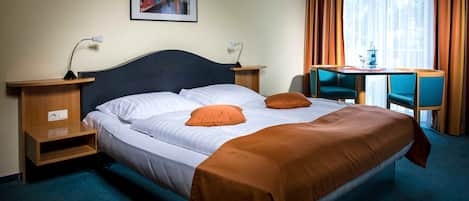 Une chambre d’hôtel comprenant un lit, deux tables de chevet, un bureau avec une chaise et une fenêtre avec des rideaux.