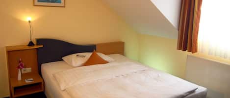 A hotel room with a single bed, a nightstand with a lamp, a framed picture on the wall, and a window with curtains.