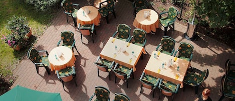 Een terras buiten met tafels en stoelen, waarvan sommige onder parasols staan.