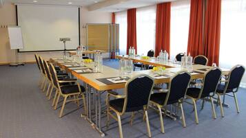 Ein Konferenzraum mit einem langen Tisch, Stühlen, einer Projektionsleinwand und einer Whiteboard-Tafel.