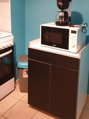 Compact kitchenette with a microwave, stove, and trash bin.