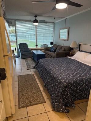 A bedroom with a large bed, a sofa, a chair, a desk, and a ceiling fan.