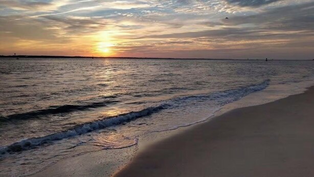 Ein Strand mit Sonnenuntergang über dem Wasser, sanfte Wellen umspülen das Ufer.
