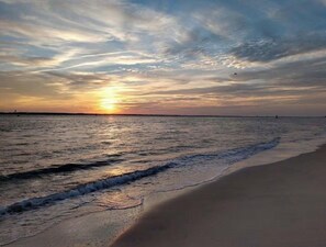 Une plage où l’on peut admirer le coucher de soleil sur l’eau, avec des vagues qui viennent doucement lécher le rivage.