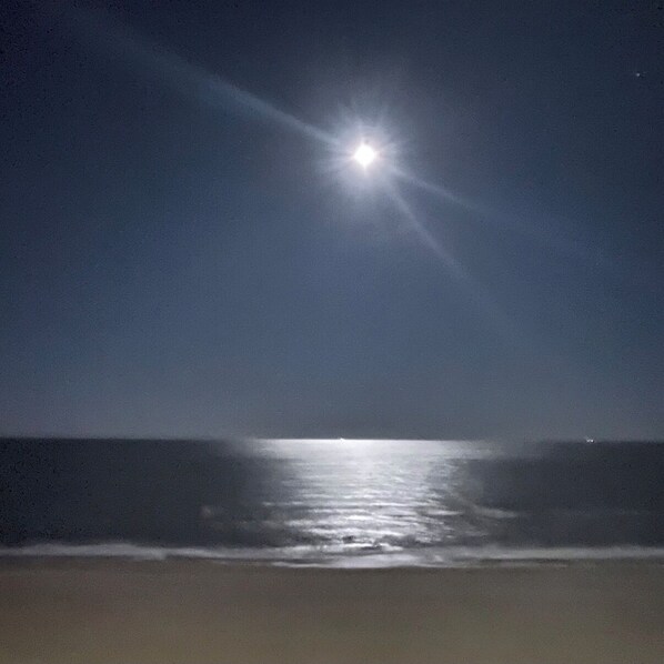 A beach scene with a bright moon or sun reflecting on the water.