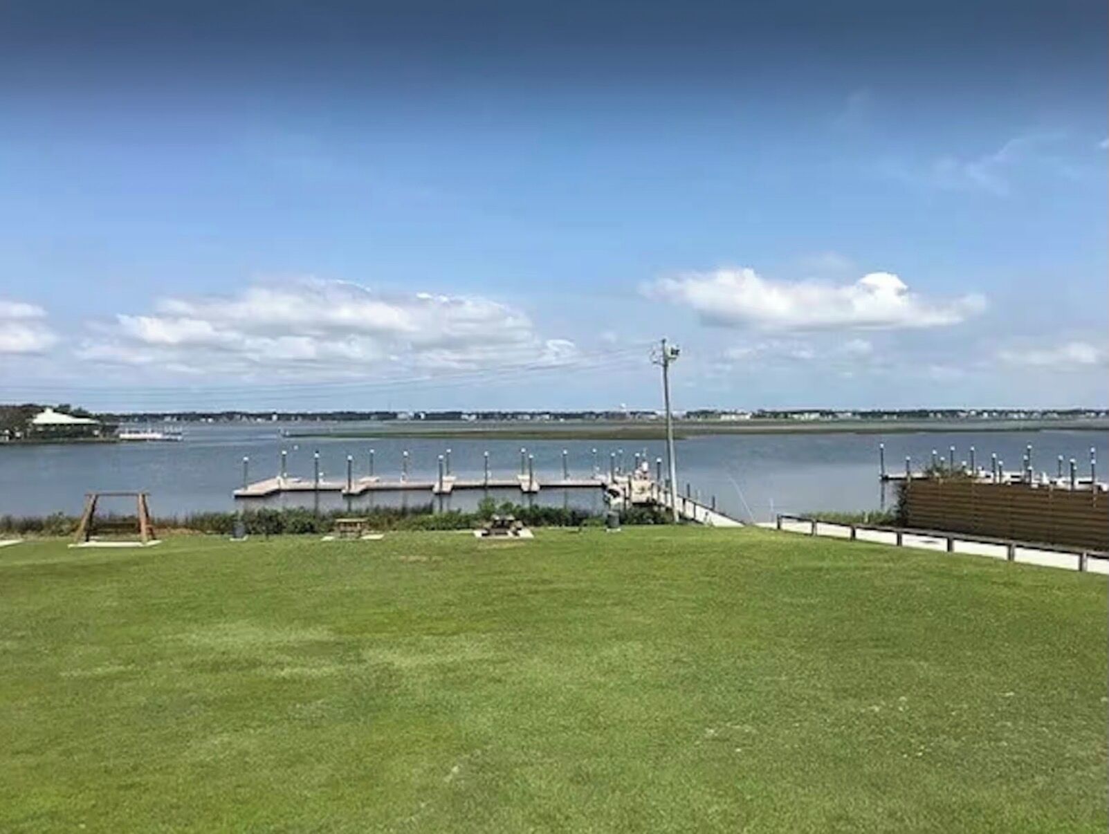 Een gazon met een steiger die in het water reikt, een schommel en een lantaarnpaal.