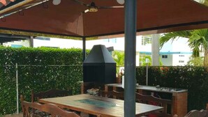 An outdoor patio with a wooden table and chairs, a barbecue grill, and a covered seating area with a ceiling fan. - Tierra Linda Girardot (Girardot)