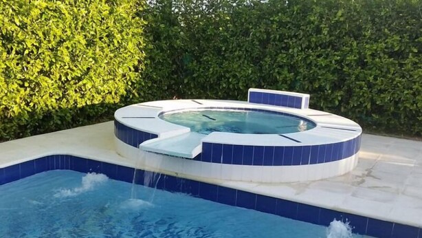 A hot tub with a blue and white tiled design, surrounded by a pool and a hedge. - Tierra Linda Girardot (Girardot)