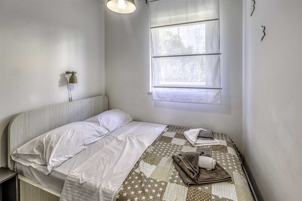 Un lit simple avec une tête de lit blanche, une courtepointe à motifs étoilés et une fenêtre avec des stores blancs.