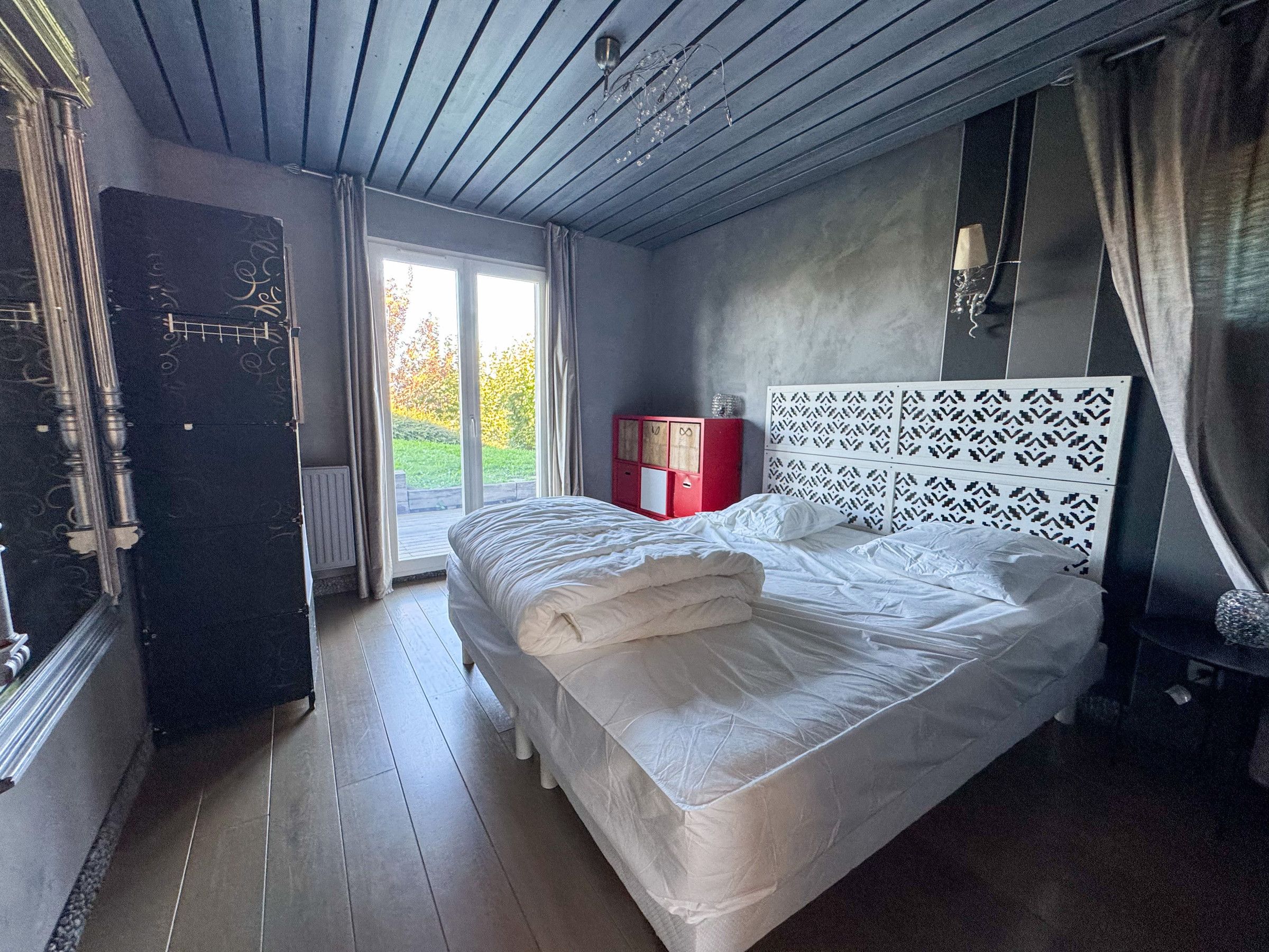 Ein Schlafzimmer mit einem Bett, einem Fenster, einem roten Schrank und einem verzierten Kopfteil.