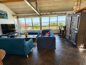 Een woonkamer met een televisie, bank en uitzicht op zee.