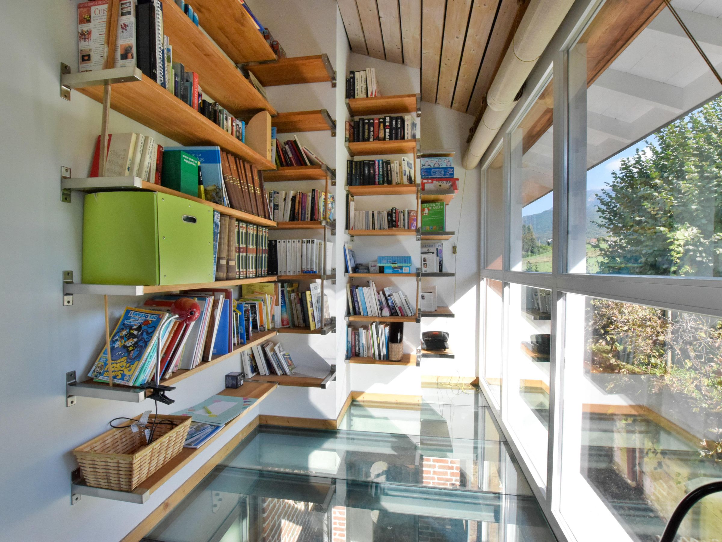 Une bibliothèque moderne dotée d’étagères et d’un plancher en verre, offrant une vue sur l’extérieur.