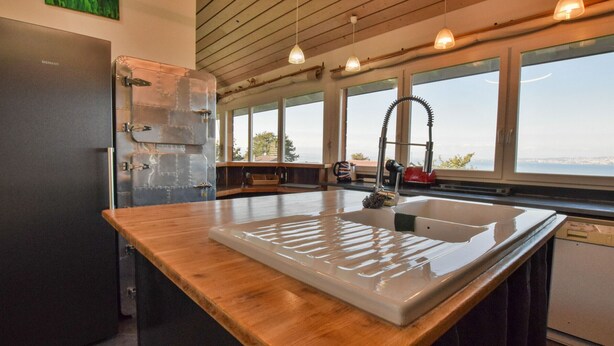 Una cocina moderna con encimera de madera, electrodomésticos de acero inoxidable y ventanas amplias con vistas al exterior.