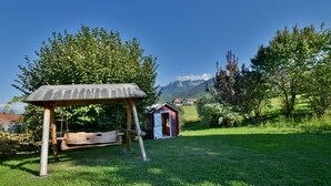 A wooden swing set in a grassy area with a small red building in the background and mountains in the distance. - Spacious villa with terrace and garden, pets and parking allowed (Lugrin)