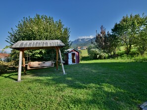 A wooden swing set in a grassy area with a small red building in the background and mountains in the distance. - Spacious villa with terrace and garden, pets and parking allowed (Lugrin)