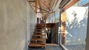 Una escalera moderna con escalones de madera y barandillas de metal, que lleva a un nivel superior con vistas al exterior.