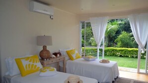 Une chambre d’hôtel avec deux lits, une fenêtre avec des rideaux, une lampe et une vue sur un jardin.