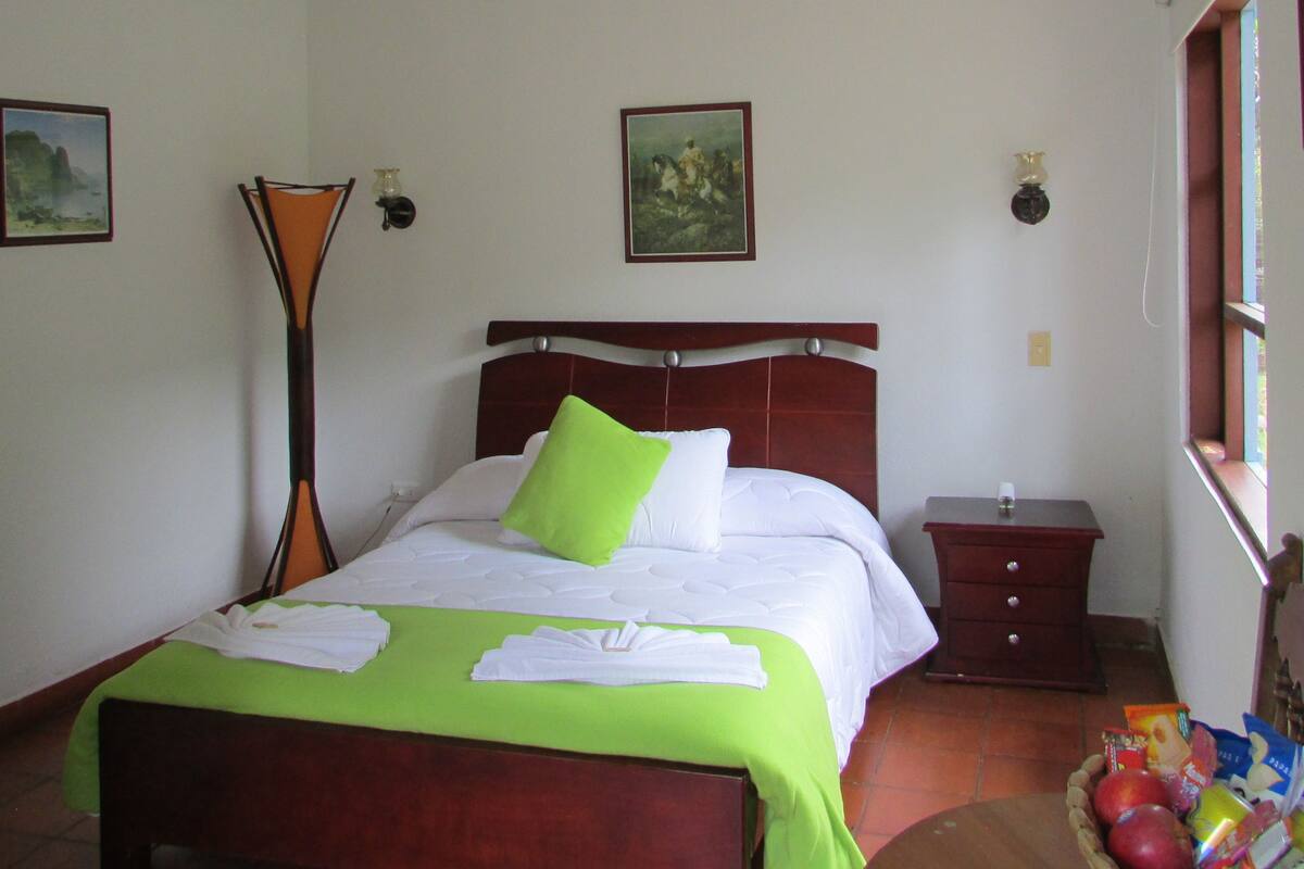 Een hotelkamer met een bed, nachtkastje, lamp en raam.