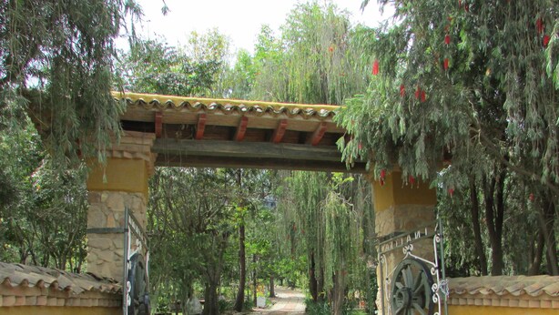 A cobblestone pathway leading through a garden with a stone archway and a decorative gate.